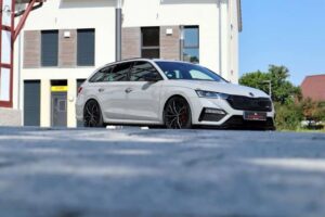 Weißer Skoda Kombi parkt vor modernem Gebäude.