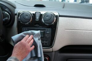 Eine Hand wischt das Armaturenbrett eines Autos mit einem Tuch ab.
