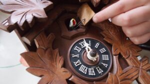 Detailaufnahme einer Kuckucksuhr mit einem Finger, der einen Mechanismus berührt.