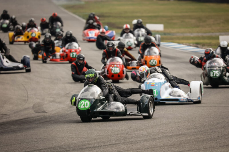 Rennszene mit mehreren Seitenwagenmotorrädern auf der Strecke.