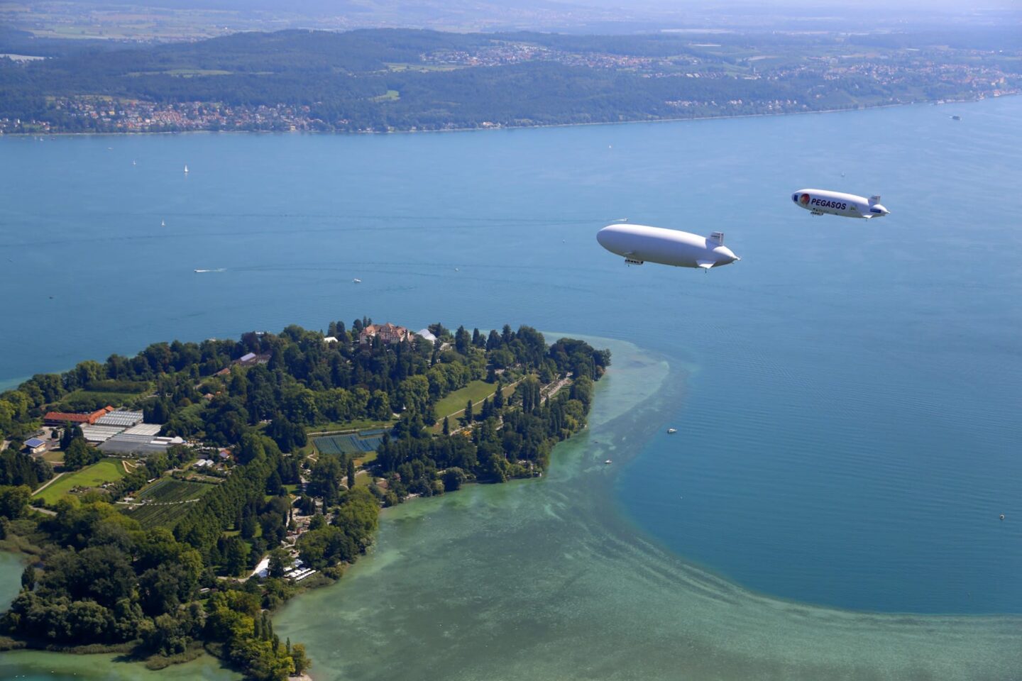 Luftaufnahme von zwei Luftschiffen über einem See und einer grünen Insel.