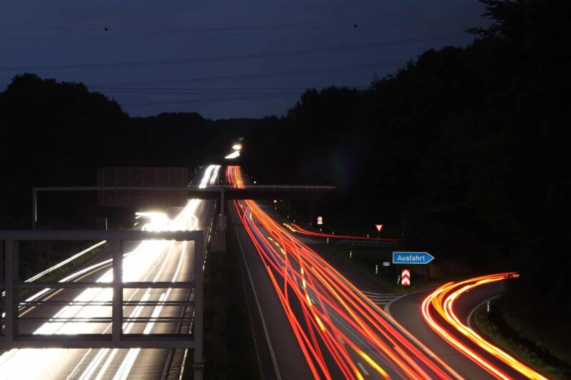 Nachtaufnahme einer Autobahn mit Lichtspuren von Fahrzeugen und einem Ausfahrtsschild.