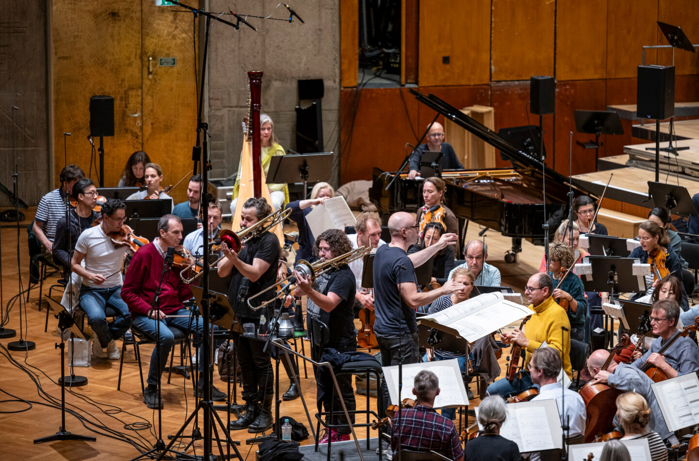 Orchesterprobe mit Musikern in einem Saal, verschiedene Instrumente und Notenständer sichtbar.