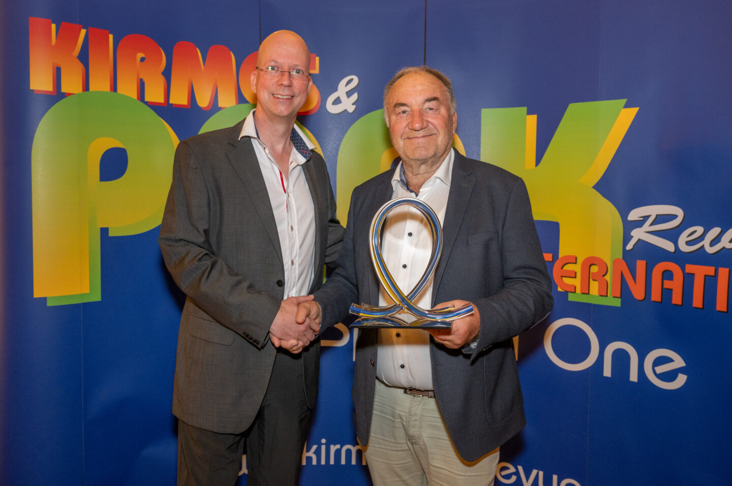 Zwei Männer schütteln sich die Hände vor einer bunten Hintergrundwand.