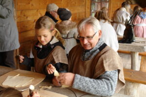Ein älterer Mann und ein Mädchen arbeiten an einem Tisch in einer Holzwerkstatt.