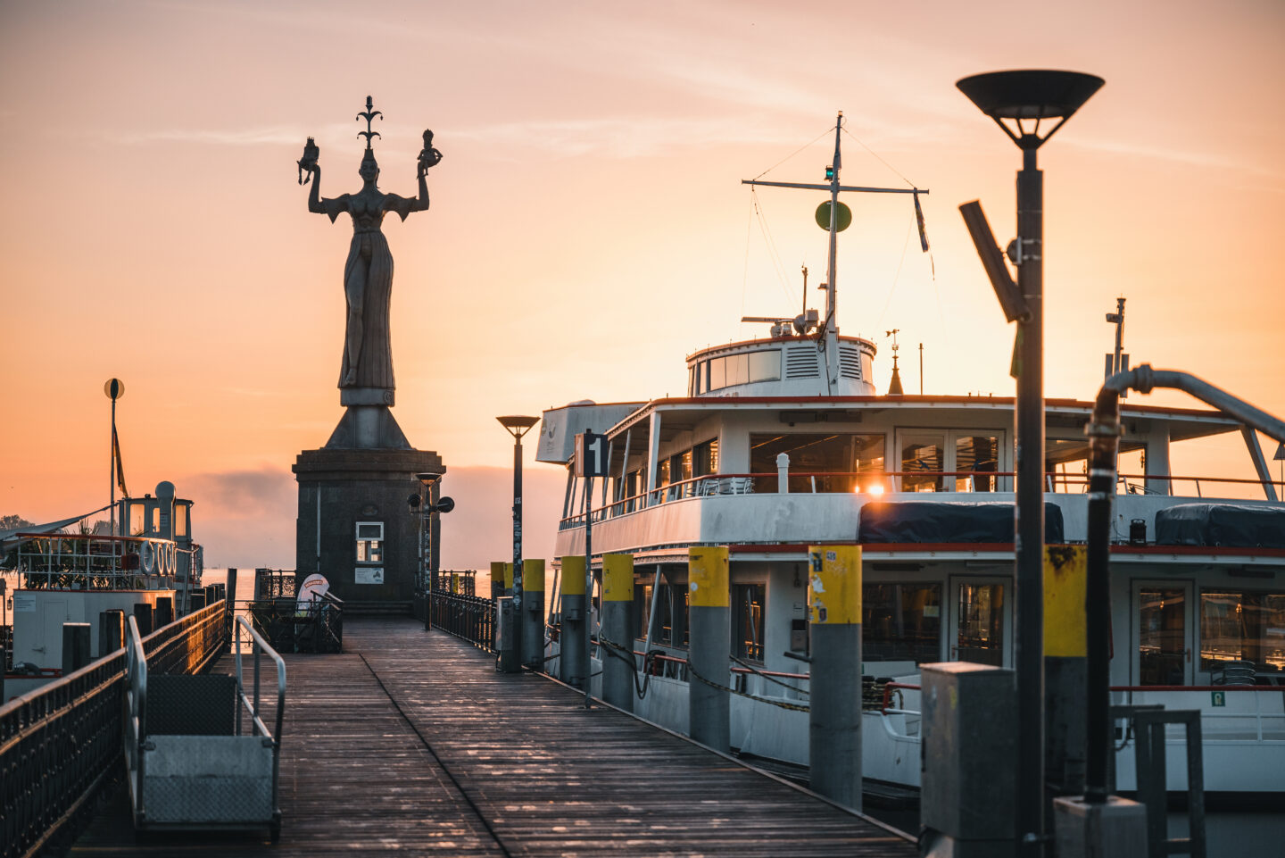 Hafen mit Statue und Schiff bei Sonnenuntergang.