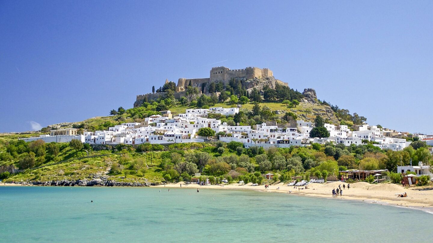 Blick auf eine Küstenlandschaft mit weißen Häusern und einer Burg auf einem Hügel.