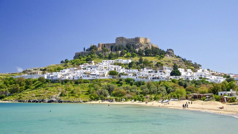 Blick auf eine Küstenlandschaft mit weißen Häusern und einer Burg auf einem Hügel.
