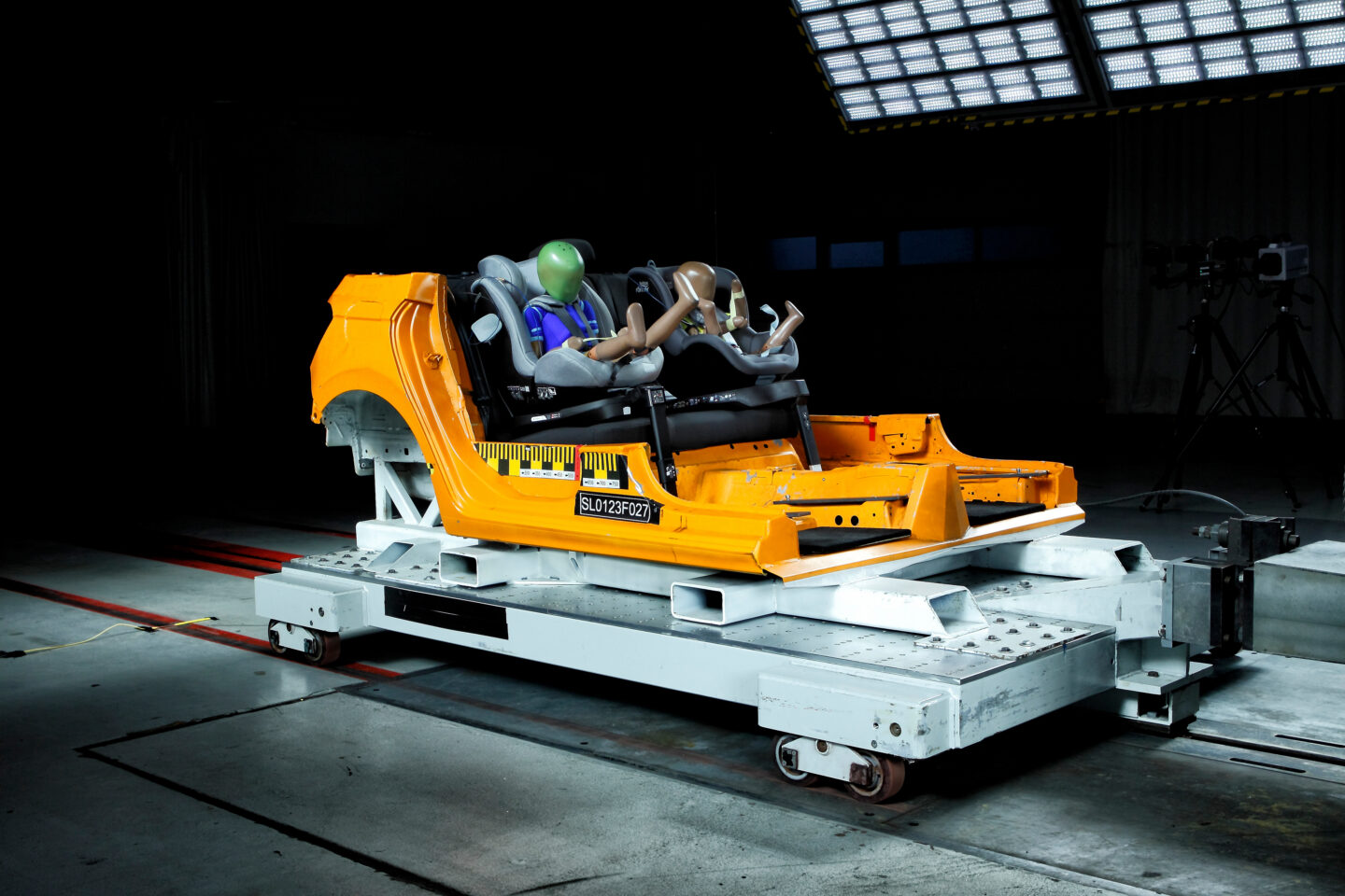 Testeinrichtung mit Dummy-Personen in einem gelben Fahrzeugrahmen.
