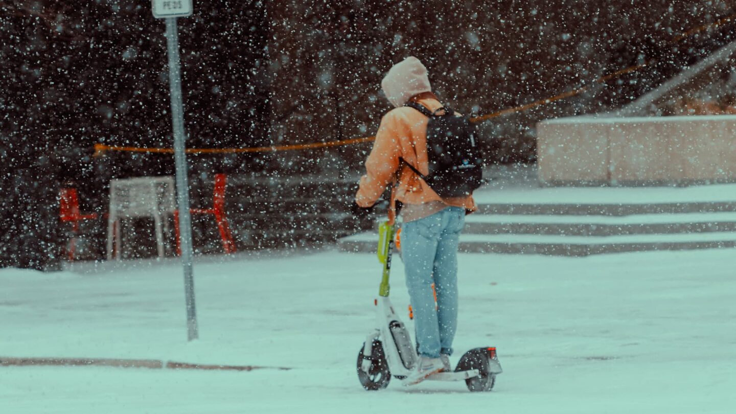 Person auf einem E-Scooter im Schnee mit winterlicher Kleidung.