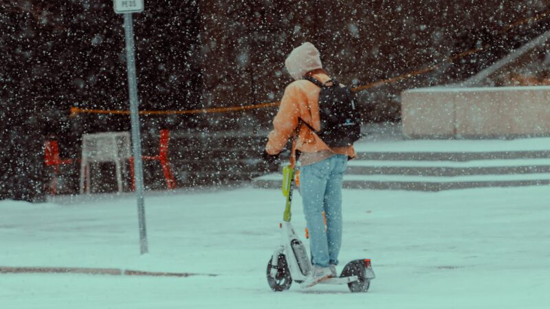 Person auf einem E-Scooter im Schnee mit winterlicher Kleidung.