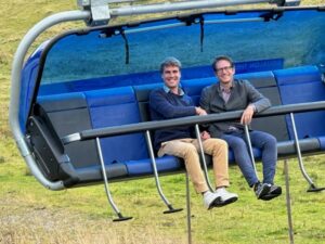 Zwei Männer sitzen in einer Seilbahn und lächeln.