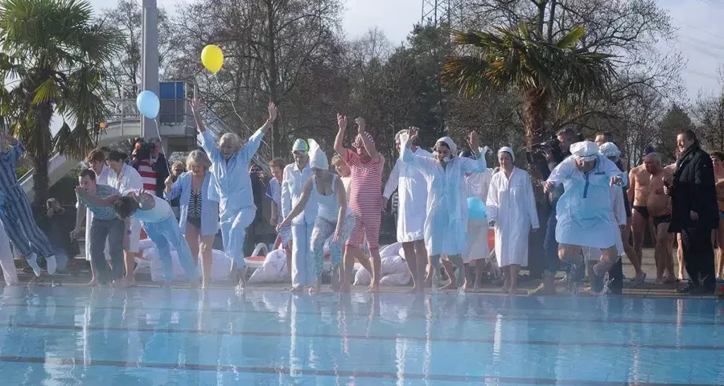 Menschen in Bademänteln und Badekleidung feiern am Pool mit Luftballons.