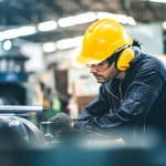 Industrieingenieure mit Schutzhelmen arbeiten in einer Schwerindustrie-Produktionsfabrik. Industriearbeiter in einer Fabrikhalle. Ein Mann bei der Arbeit in einer Industriefabrik. Sicherheitskonzept: Sicherheit steht an erster Stelle.