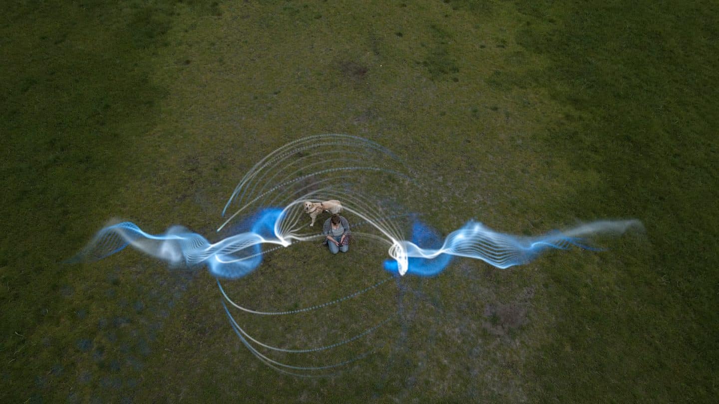 "Wir hör'n uns, wenn ich tot bin! - Trauer und KI": Montage: Eine Frau sitzt mit einem Hund auf einer grünen Wiese. Darüber schweben grafische Audiowellen der Künstlichen Intelligenz.
