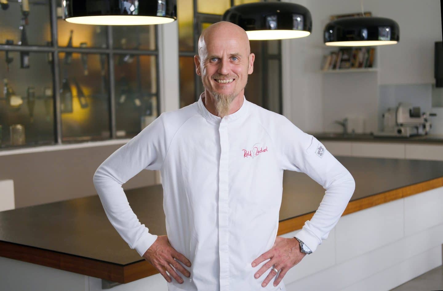 WISO-Dokumentation: Get rich: Erfolg durch Dropshipping?": Koch Ralf Zacherl steht in der Showküche seines Restaurants in Berlin. Er trägt eine klassische weiße Kochjacke, hat die Arme in die Hüften gestemmt und schaut lächelnd in die Kamera.