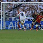 Szene aus dem EM-Spiel Deutschland gegen Spanien: Der Ball fliegt in Richtung des spanischen Tores, Spieler beider Mannschaften im Fokus, darunter das kontroverse Handspiel, das zu Diskussionen führte.