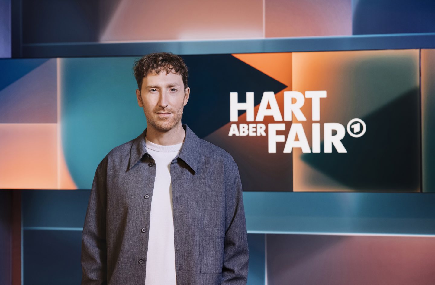 Louis Klamroth, Moderator der ARD-Talkshow „hart aber fair“, steht vor dem Studiohintergrund mit dem Sendungslogo.