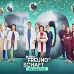 Das Ensemble der Serie 'In aller Freundschaft – Die jungen Ärzte' posiert vor einer großen, silbernen '10', die von Ballons und Konfetti umgeben ist. Die Schauspielerinnen und Schauspieler stehen lächelnd in ihrer typischen Krankenhauskleidung oder Alltagsmode, während im Vordergrund eine Torte mit brennenden Kerzen gehalten wird. Der grüne Hintergrund und das große Jubiläumslogo betonen das 10-jährige Bestehen der Serie. Personen: V.l.n.r.: Assistenzarzt Florian Osterwald (Lion Wasczyk), Mikko Rantala (Luan Gummich), Dr. Julia Berger (Mirka Pigulla), Dr. Matteo Moreau (Mike Adler), Dr. Leyla Sherbaz (Sanam Afrashteh), Dr. Ben Ahlbeck (Philipp Danne), Dr. Marc Lindner (Christian Beermann), Prof. Dr. Karin Patzelt (Marijam Agischewa), Sofia Galura (Olivia Papoli-Barawati), Oliver ,,Olli" Probst (Arne Kertész), Tamar Hummel (Linda Kummer), Dr. Elly Winter (Juliane Fisch), Ivo Maric (Jakob D´Aprile) und Klinikdirektor Wolfgang Berger (Horst Günter Marx).