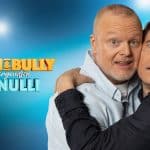 Stefan Raab und Michael Bully Herbig umarmen sich humorvoll vor einem blauen Hintergrund mit dem Schriftzug „Stefan & Bully gegen irgendson Schnulli“. Der Titel der RTL-Show ist in auffälligen Farben gestaltet.