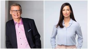 Günther Jauch (links) in einem dunklen Anzug mit rosa Hemd und Pinar Atalay (rechts) in einer hellblauen Bluse stehen jeweils vor neutralem Hintergrund. Beide blicken freundlich in die Kamera.