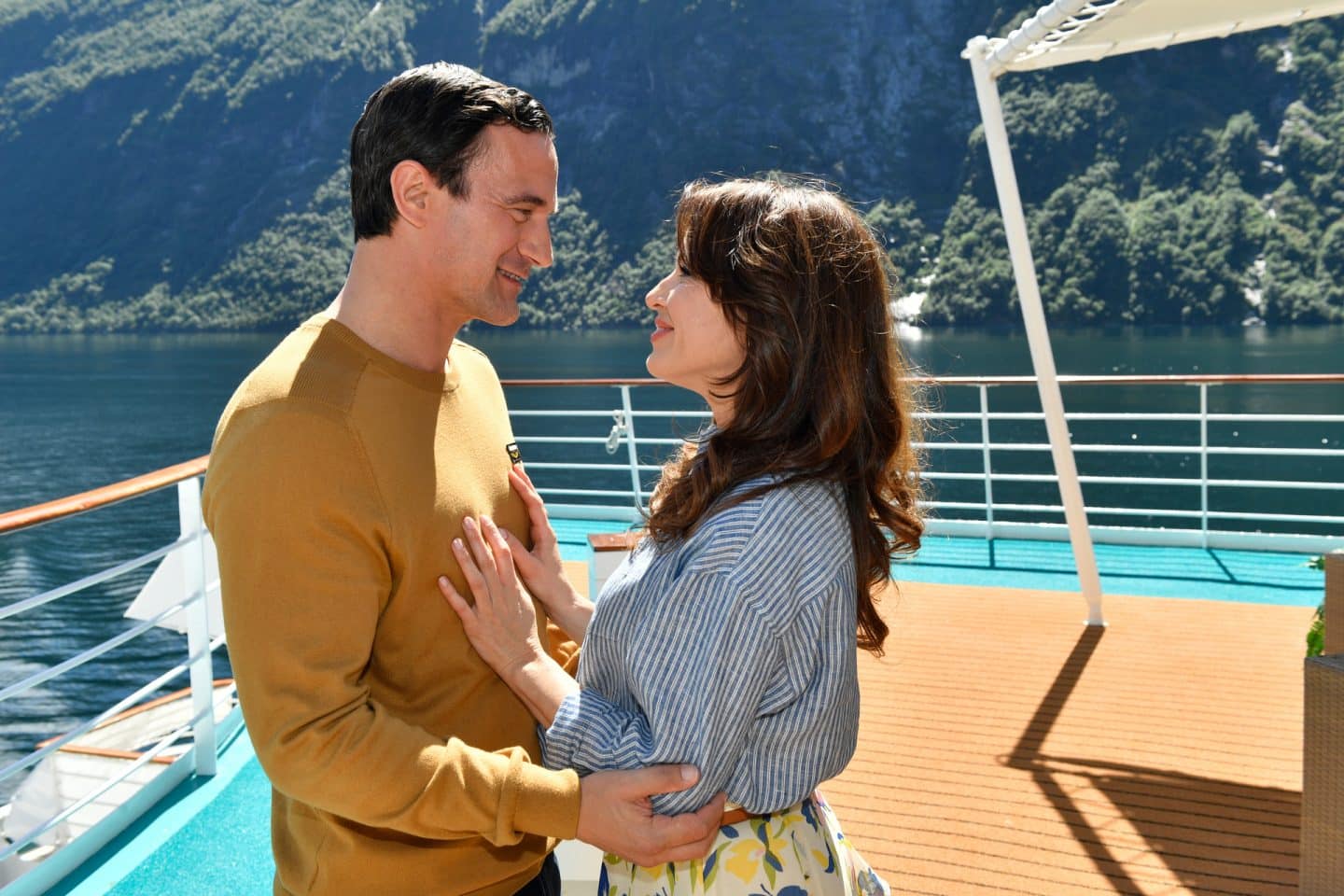 "Das Traumschiff: Hudson Valley": An Deck des Schiffs: Frederike Hansen (Natalie Avelon) und Daniel Peterson (Sönke Möhring) stehen sich lächelnd gegenüber. Im Hintergrund ist die Küste zu sehen.