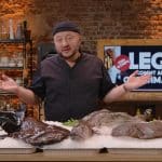 Sebastian Lege, der Foodexperte aus der VOX-Sendung „Lege kommt auf den Geschmack“, steht in einer rustikalen Studioküche. Vor ihm auf Eis liegen verschiedene große Fische, während er gestikulierend und mit offener Haltung in die Kamera blickt. Im Hintergrund ist ein Bildschirm mit dem Titel der Sendung und einem „Fish & Chips“-Logo zu sehen.
