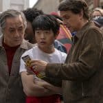 Jackie Chan, Ben Wang und Ralph Macchio in einer Szene aus ‚Karate Kid: Legends‘ – gemeinsames Studium eines Flyers in einer belebten Umgebung.