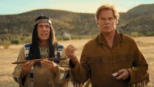 Michael Bully Herbig als Häuptling Abahachi und Christian Tramitz als Ranger stehen in einer typischen Wildwest-Landschaft. Abahachi hält eine traditionelle Friedenspfeife, während Ranger irritiert eine brennende Streichholzschachtel betrachtet. Die Szene ist humorvoll inszeniert und vermittelt den typischen Stil von „Das Kanu des Manitu“. Im Hintergrund sind Wüstenhügel und blauer Himmel zu sehen.