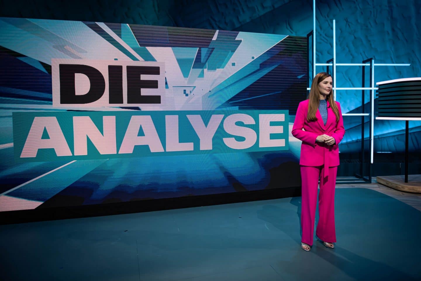 Linda Zervakis enthüllt die „Fake News“ 2024 – ProSieben mit TV-Premiere! 1 Linda Zervakis im auffälligen pinken Hosenanzug steht vor einem großen Bildschirm im Studio. Auf dem Bildschirm prangt der Schriftzug „DIE ANALYSE“ in großen Buchstaben. Das Setting ist modern und in blauen Farbtönen gehalten.