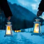 Zwei Personen halten leuchtende Laternen bei der Laternen-Weihnachtswanderung in der Ravennaschlucht. Der verschneite Pfad, die stimmungsvollen Laternen und die winterliche Bergkulisse schaffen eine festliche Atmosphäre.