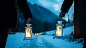 Zwei Personen halten leuchtende Laternen bei der Laternen-Weihnachtswanderung in der Ravennaschlucht. Der verschneite Pfad, die stimmungsvollen Laternen und die winterliche Bergkulisse schaffen eine festliche Atmosphäre.