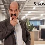 Christoph Maria Herbst in seiner Rolle als Stromberg, humorvoll posierend in einem modernen Büro. Im Hintergrund ist der Schriftzug "Stromberg" zu sehen, der die bekannte Comedy-Serie repräsentiert.