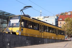 Ein gelber Triebwagen der Stuttgarter Zahnradbahn steht an der Haltestelle Marienplatz. Im Hintergrund sind moderne Gebäude und Herbstbäume zu sehen, die das Stadtbild von Stuttgart prägen. Die Bahn gehört zur dritten Generation und ist ein Symbol für die Verbindung von Tradition und Fortschritt im Nahverkehr