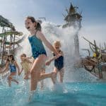 Fröhliche Kinder spielen im Svalgurok-Bereich von Rulantica, umgeben von thematisierten Wasserrutschen und Attraktionen bei strahlendem Sonnenschein.