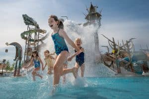 Fröhliche Kinder spielen im Svalgurok-Bereich von Rulantica, umgeben von thematisierten Wasserrutschen und Attraktionen bei strahlendem Sonnenschein.