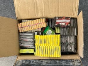 Offener Karton mit mehreren Packungen Feuerwerkskörper, darunter Böller in gelben, schwarzen und roten Verpackungen, die eng gestapelt sind.