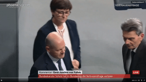 Screenshot aus einer Phoenix-Live-Übertragung im Bundestag. Im Vordergrund Bundeskanzler Olaf Scholz, der nach unten schaut, während er mit Rolf Mützenich vorbeigeht. Im Hintergrund Saskia Esken, die sichtlich irritiert wirkt und in Richtung der beiden schaut. Einblendung unten zeigt: "Kommentar: Gerd-Joachim von Fallois - Bundeskanzler Scholz hat im Bundestag di