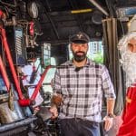 Ein Lokführer in traditioneller Uniform steht neben einer als Nikolaus verkleideten Person im Führerstand einer historischen Dampflok. Die Szene spielt im Rahmen der Sonderfahrt des Dampfzugs zum Weihnachtsmarkt in Ottenhöfen. Im Hintergrund sind technische Details der Dampflok und eine grüne Außenlandschaft erkennbar.