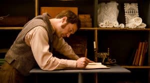 Vincent Redetzki als Levi Strauss, der an einem Schreibtisch sitzt und in ein Buch schreibt. Im Hintergrund sind Regale mit Stoffen und Büchern zu sehen.