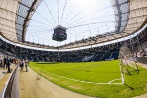 „Das Stadion in Frankfurt, bekannt als Deutsche Bank Park, mit einem Blick auf das Spielfeld, die leeren Tribünen und die beeindruckende Dachkonstruktion unter blauem Himmel.“