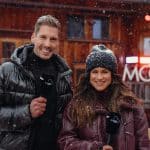 Steffi Brungs und Norman Langen stehen vor dem MooserWirt in St. Anton am Arlberg, halten Mikrofone in der Hand und lächeln in die Kamera. Im Hintergrund ist die beleuchtete Fassade der berühmten Skihütte zu sehen, während es leicht schneit.