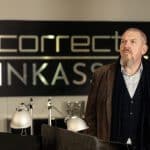 Freddy Schenk (Dietmar Bär) steht nachdenklich im Büro der fiktiven Firma Correct Inkasso. Hinter ihm ist das Firmenschild mit dem Schriftzug „Correct Inkasso“ deutlich zu sehen. Die Szene vermittelt die ernste Atmosphäre der Ermittlungen im Umfeld des umstrittenen Inkasso-Unternehmens.