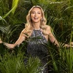 Anna-Carina Woitschack steht lächelnd in einem funkelnden silbernen Kleid zwischen grünen Dschungelpflanzen und wirkt strahlend und energiegeladen.