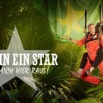 Teaserbild für die RTL-Show "Ich bin ein Star – Holt mich hier raus!". Im Vordergrund schwingen zwei Personen in roten Dschungelanzügen, befestigt an Seilen, durch die tropische Vegetation. Im Hintergrund sind Palmenblätter und ein großes, leicht verschwommenes Banner in den Farben Grün und Gelb zu sehen. Der Schriftzug der Show mit einem Stern als Designelement steht prominent links im Bild.