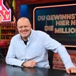 Stefan Raab sitzt lächelnd an einem Schreibtisch in einem TV-Studio. Im Hintergrund ist ein Bildschirm mit dem Schriftzug „Du gewinnst hier nicht die Million !!!“ zu sehen, der Titel seiner neuen RTL-Show.