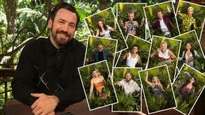 Jan Köppen sitzt lächelnd vor einer Collage der 17 Dschungelcamp-Kandidaten 2025, die jeweils in kleinen Rahmen dargestellt und von tropischen Pflanzen umgeben sind.
