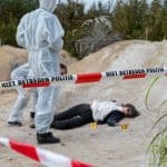 "Aktenzeichen XY... Ungelöst": Nachgestellte Szene: Rot-weiß gestreiftes Absperrband schirmt einen Tatort ab. Dahinter liegt eine tote Frau in den Dünen auf dem Boden. Neben ihr stehen zwei Personen in weißen Anzügen von der Spurensicherung und schauen sie an.
