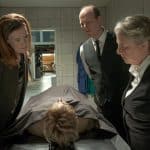Die Bestatter Frau Bleckmann (Regine Hentschel) und Herr Töteberg (Stephan A. Tölle) stehen in einem kalten Raum neben Friseurin Grit Hartmann (Julika Jenkins), während sie gemeinsam eine zugedeckte Leiche auf einer Bahre betrachten.