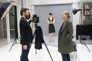 "Die Chefin - True Crime": In einem weißen Fotostudio befragt Vera Lanz (Katharina Böhm) den schwarz gekleideten Fotografen Ulf Brandt (Thomas Wodianka). Er hat eine Hand an seiner Kamera, die auf einem Stativ steht und auf eine ausgerollte graue Leinwand gerichtet ist. Dort steht eine Schaufensterpuppe mit verschränkten Armen, gekleidet in ein kurzes schwarzes Kleid und eine schwarze Baskenmütze.